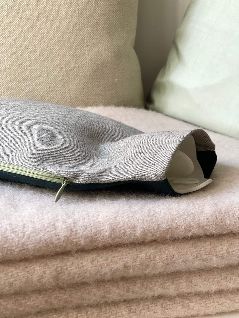 Gemütliche Szene mit Wärmflaschenbezug JULZE in Petrol und Beige-Grau auf rosa Decke – gefertigt aus reinen Naturfasern von HETTI. Berlin.