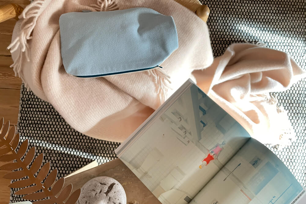 Wohnliches Setting mit Wärmflasche im Bezug NICK, rosa Decke, Kunstbuch und Teppich – hochwertiges Accessoire für gemütliche Stunden.